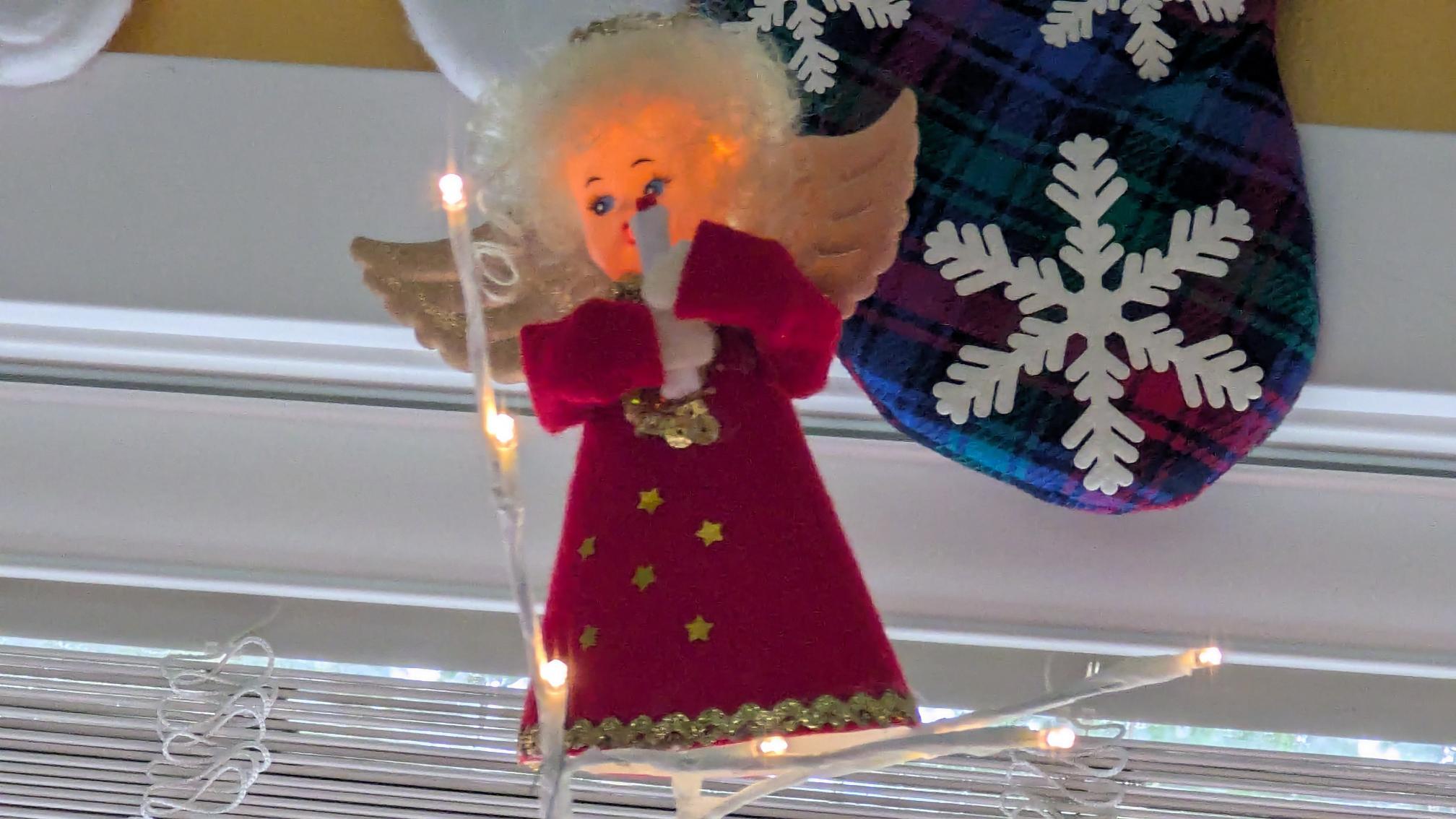 Scruffy little angel in red holding a candle on top of a birch christmas tree.