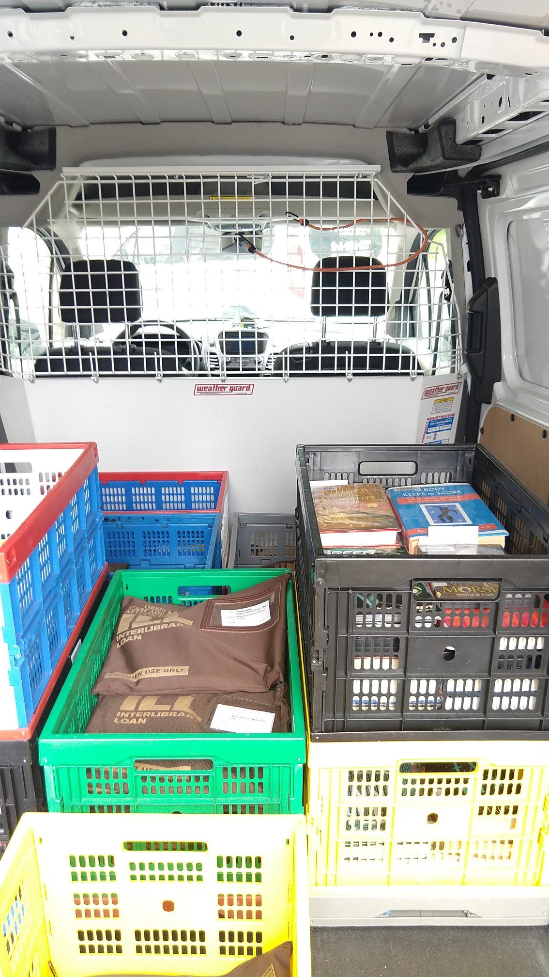 Back of a work van with a steel grate between the driver and the back area where the books are kept. There are half a dozen milk crates filled with books and other library materials.