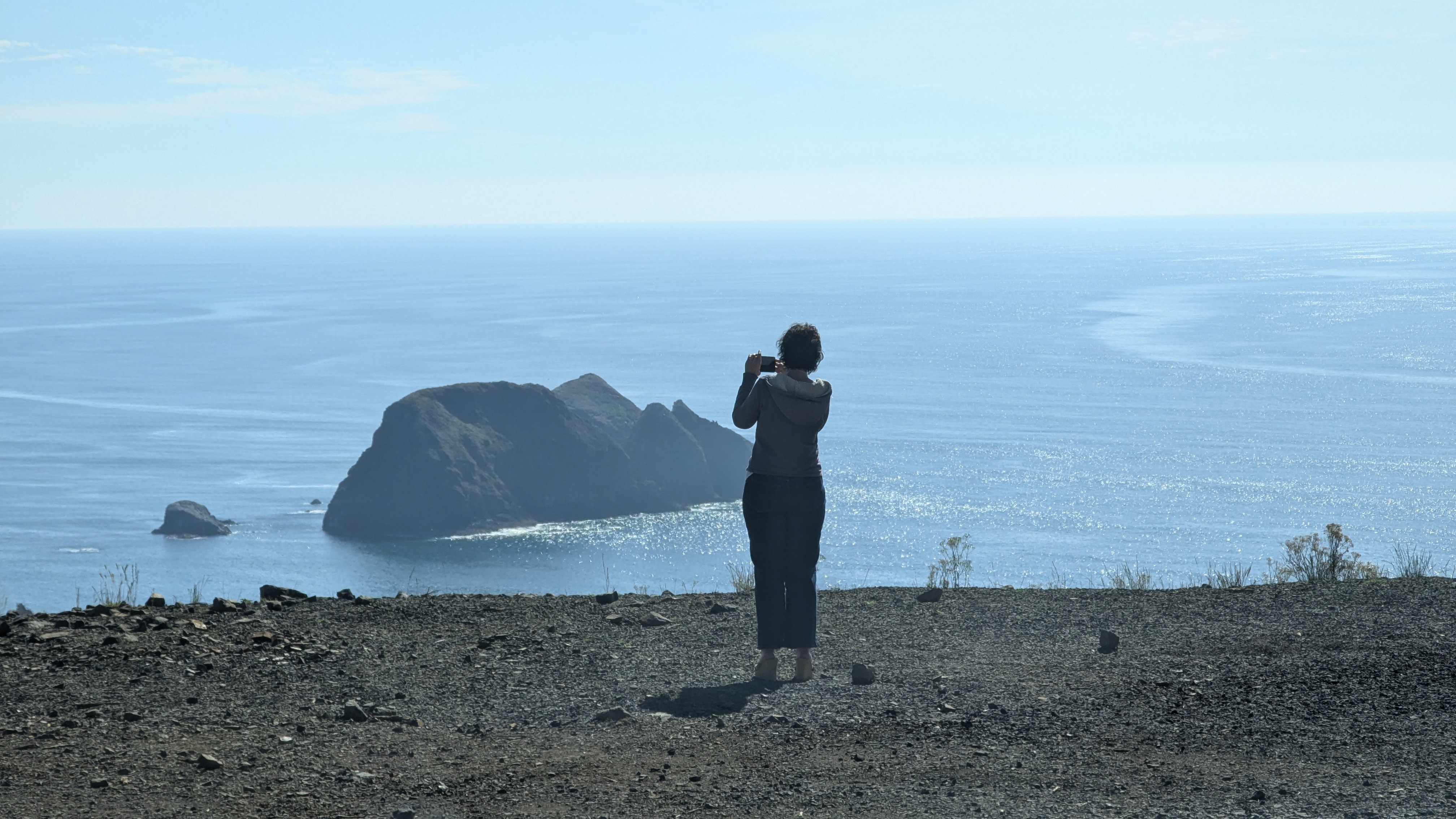 Stacy standing on a bluff overlooking the Pacific Ocean and taking a picture.