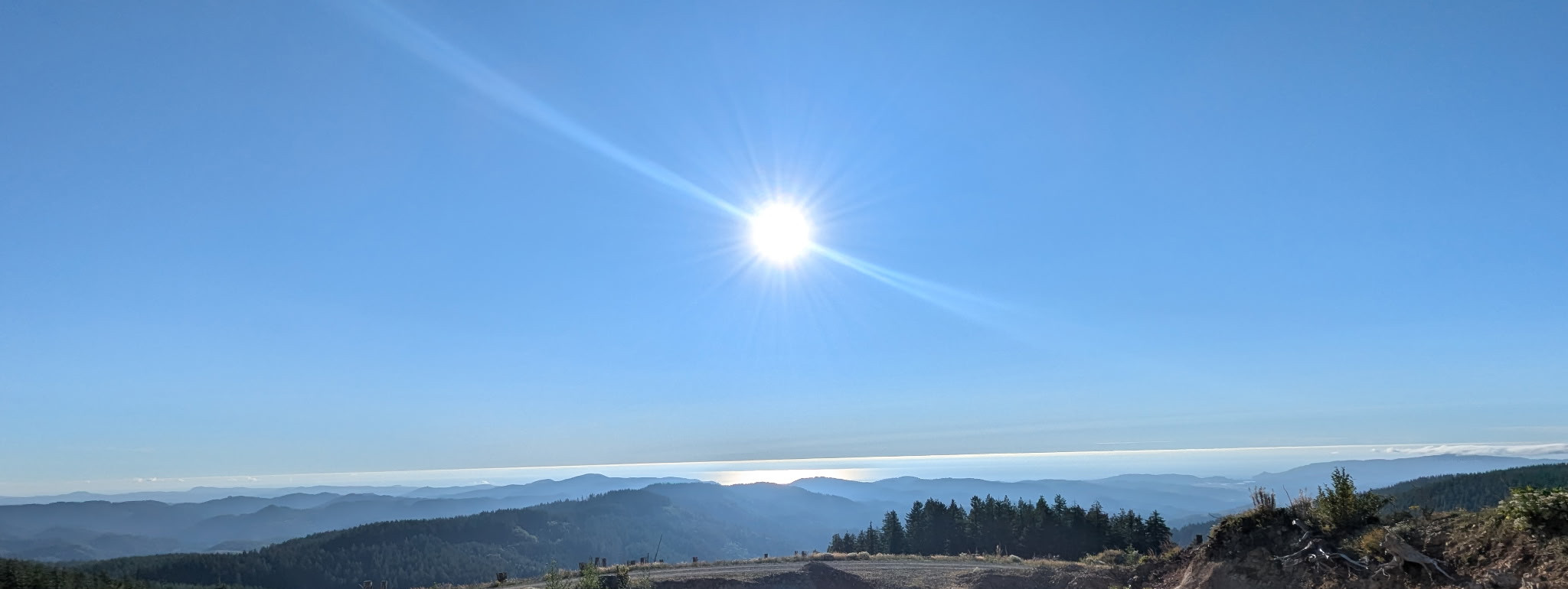 Blue skies, shadowed mountains, giant sun, bright sea.