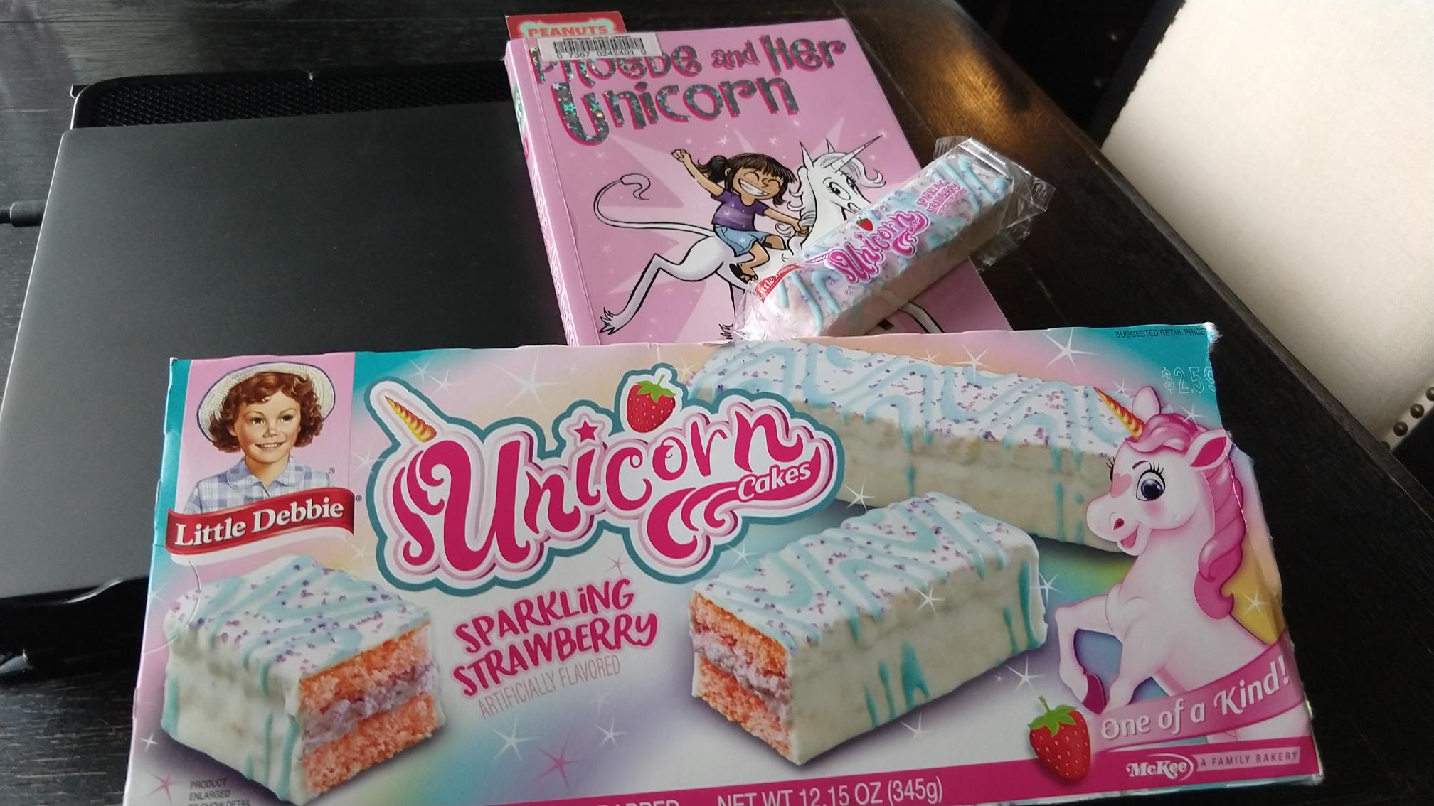 Box of rainbow colored unicorn cakes nestled right up to the book Phoebe and Her Unicorn.