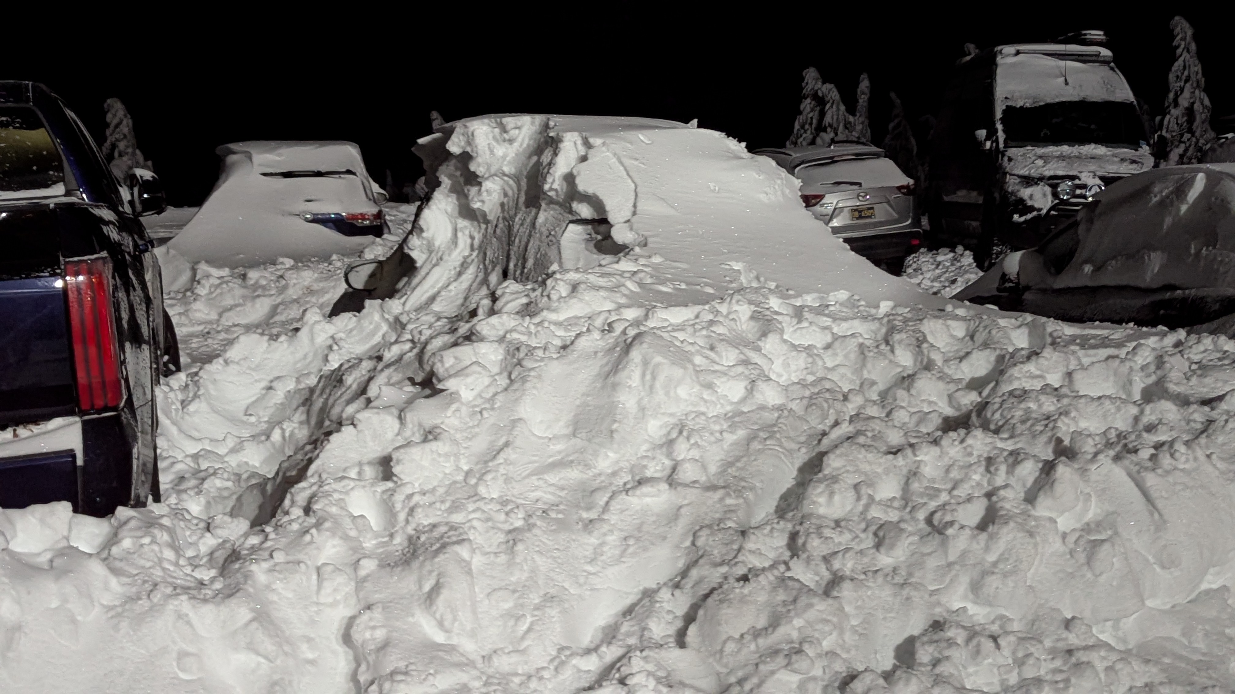 Winter alpine setting. Nighttime. Cars buried under feet of snow, identifiable only as giant lumps of snow.