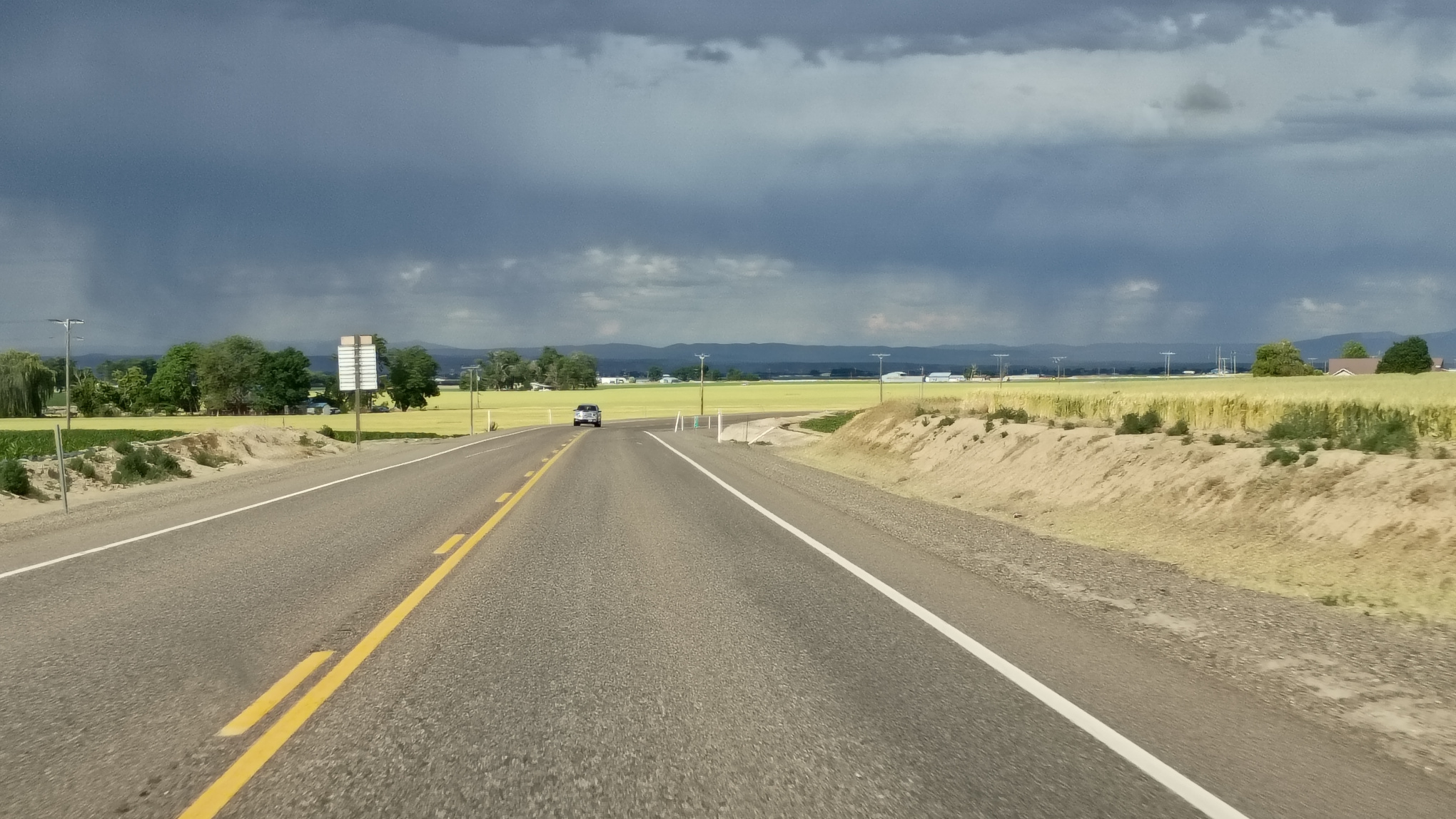 Highway through western Oregon dark blue storm clouds above and golden grass below.
