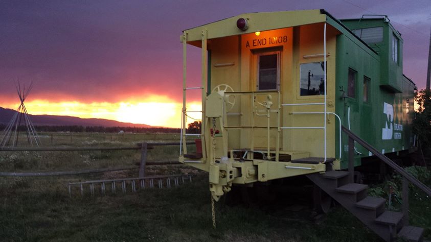 Yellow caboose with deep, dark orange sunset behind it and the Wallowas rising to the left.
