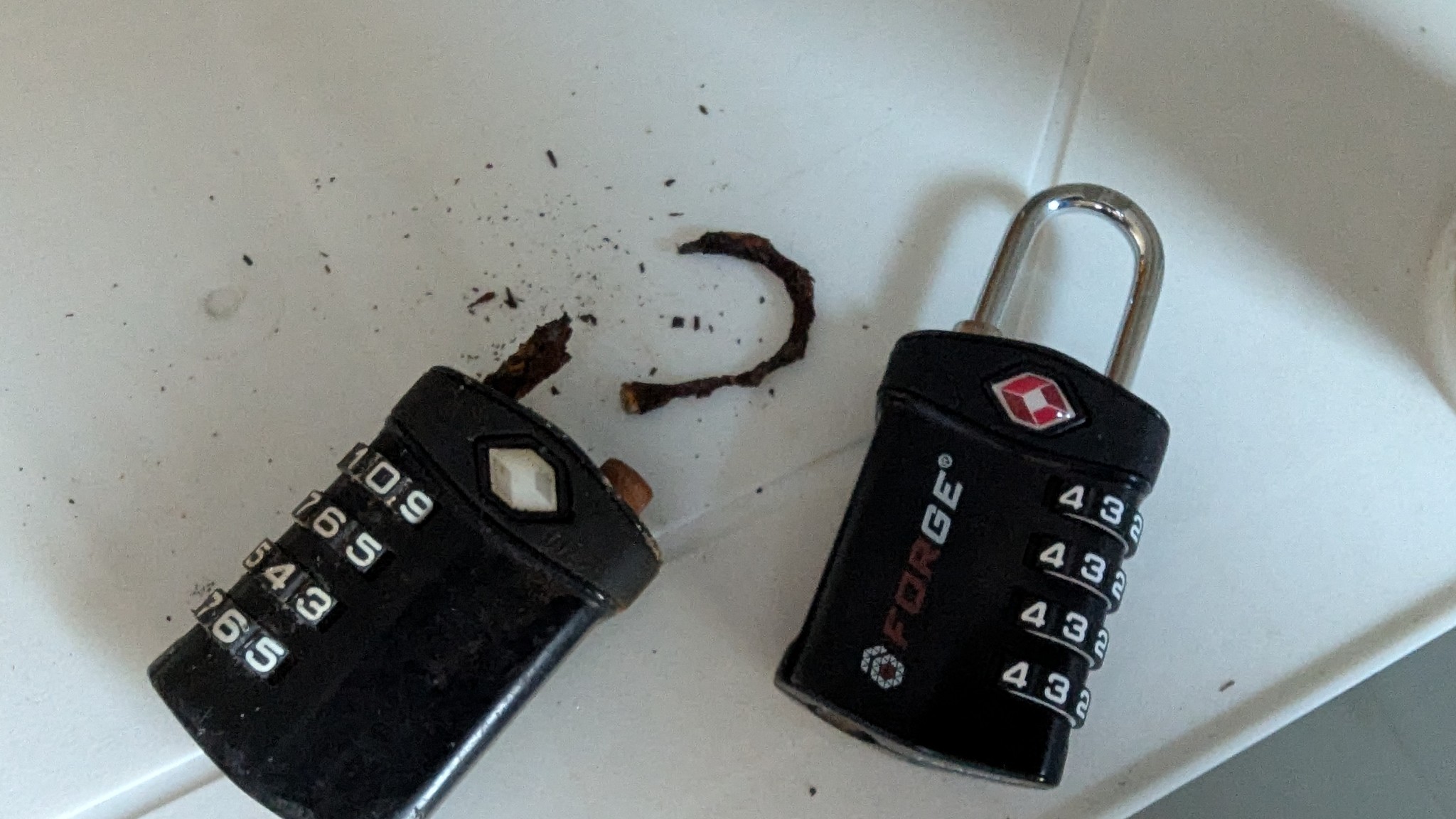 Two luggage locks. The one on the left has has almost no metal left, and the metal that is left is brown and crumbling. The lock on the right is new and shiny.