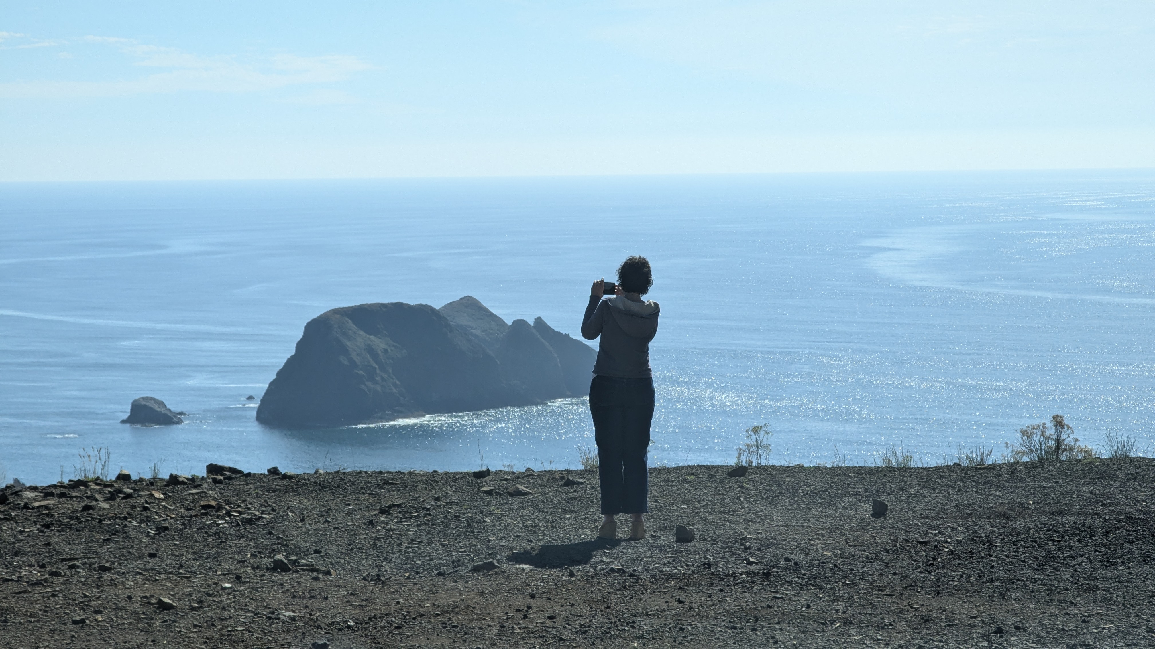 Stacy standing on a bluff overlooking the Pacific Ocean and taking a picture.